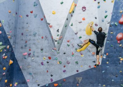 A man in activewear climbing an indoor bouldering wall with colorful holds.