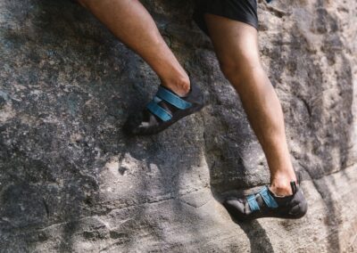 Detailed view of a rock climber's shoes gripping a rugged cliff face outdoors.