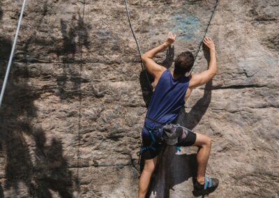 Determined man climbing a rock wall with safety harness and ropes, showcasing adventure and strength.